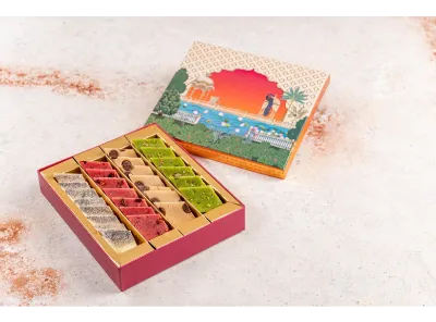 An assorted box of colorful Kaju Katli sweets in silver, pink, beige, and green varieties, neatly arranged in rows inside a festive gift box.