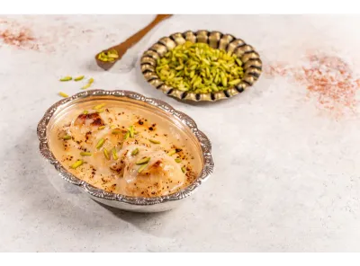 Delicious baked rasgullas soaked in creamy rabri, garnished with slivered pistachios, served in a silver bowl.