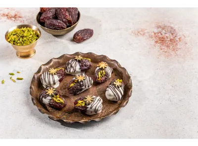 Stuffed Dates with White Chocolate Drizzle – gourmet dates filled with chopped pistachios and almonds, elegantly coated in white chocolate and topped with decorative edible flowers.