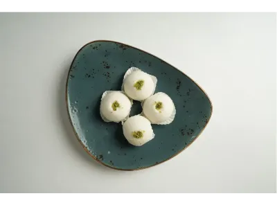 Four white Gulab Pati Sandesh sweets garnished with pistachios, placed on a dark ceramic plate