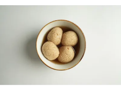Soft and spongy gur rasgullas soaked in jaggery syrup, served in a white bowl with brown rim.