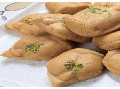 Brown Gur Sandesh sweets neatly arranged on a tray, garnished with crushed pistachios, made from jaggery and paneer