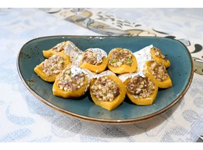 Sugarless sweets filled with a rich almond and date mixture, garnished with silver foil and dry fruits, arranged neatly on a plate.