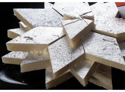 Stack of Kaju Katli sweets garnished with silver leaf on a black plate