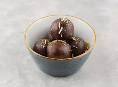 Bowl of dark brown kala jamun sweets garnished with chopped nuts, served in a blue ceramic bowl.