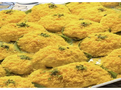 Malai Moon Indian sweets arranged on a tray, topped with saffron-colored coconut and pistachios