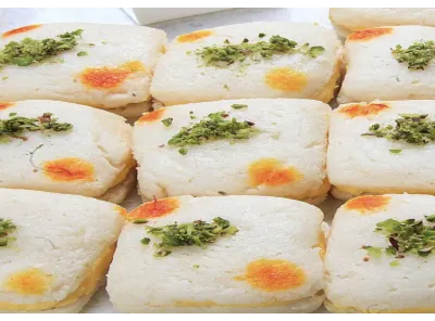 Close-up view of square-shaped Malai Sandwich sweets garnished with chopped pistachios and saffron spots on top.