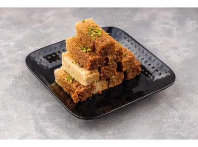 Stack of brown and white Milk Cake slices garnished with pistachios on a glossy black plate.