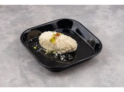 Milk cham cham dessert served on a black plate, garnished with saffron strands and chopped pistachios.