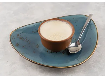 Traditional Mishti Doi served in an earthen pot on a blue ceramic plate with a spoon beside it on a grey textured surface.