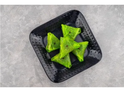 Bright green Petha Paan triangles served on a black plate, garnished with cloves and filled with sweet stuffing.