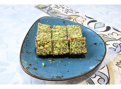 Sugarless Pista Dates Barfi topped with crushed pistachios, cut into square pieces, showcasing a vibrant green and rich texture.