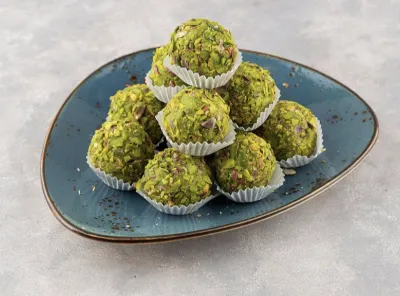 Plate of pista paan ladoos garnished with chopped pistachios, served in white paper cups