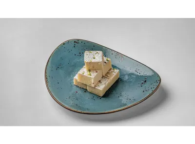 Stack of plain Mawa Barfi pieces topped with silver foil and pistachios on a blue ceramic plate.