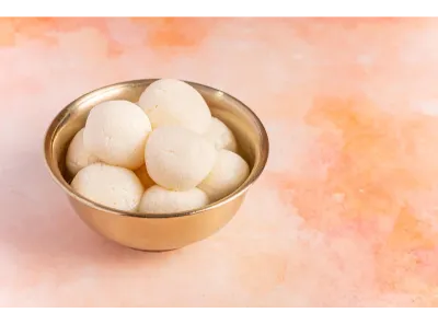 Traditional Rasgullas stacked in a brass bowl, placed on a warm peach-orange textured background.