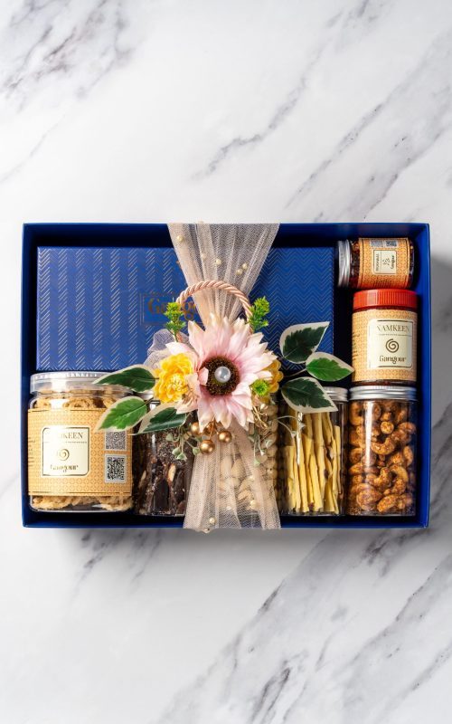 Elegant gift hamper in a blue box with assorted snacks in jars, decorated with artificial flowers